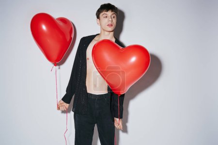 romantic young man in black open shirt holding red balloons on grey background, Valentines day