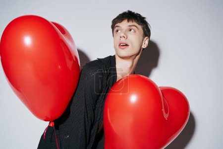 romantic man in black shirt holding red heart shaped balloons on grey background, Valentines day