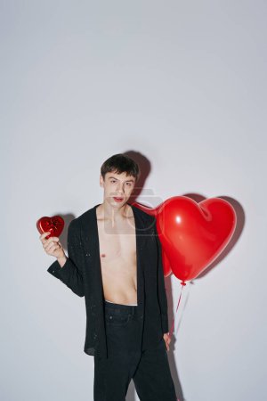 young man in shirt holding red heart shaped balloon and present on grey background, Valentines day