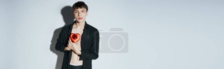 handsome man in shirt holding red heart shaped present box on grey background, Valentines day banner