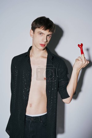 provocative young man in open black shirt showing middle finger with red balloon on grey background