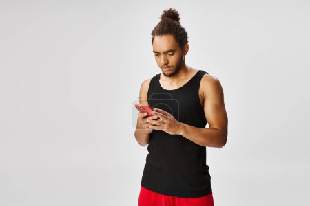 handsome african american sportsman looking at his smartphone on gray backdrop, online betting