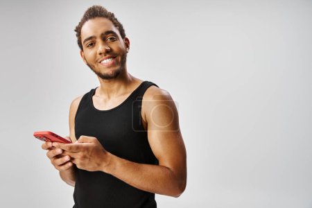 cheerful athletic african american man holding smartphone and smiling at camera, online betting