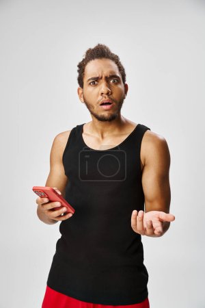 confused handsome african american man holding phone and looking at camera, online betting