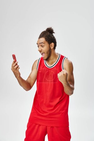 happy shocked african american man in sportwear cheering and looking at smartphone, online betting