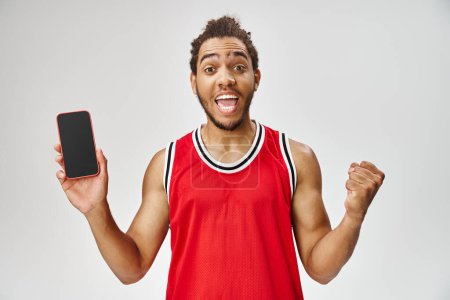 cheerful african american man in sportwear holding phone and looking at camera, online betting