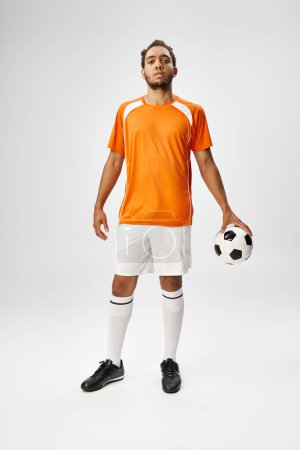 Téléchargez les photos : Beau jeune homme afro-américain en vêtements de sport posant avec le football sur fond gris - en image libre de droit