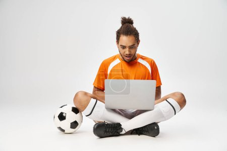 emotionale afrikanisch-amerikanische Mann Blick auf Laptop sitzt auf dem Boden neben Fußball, Online-Wetten