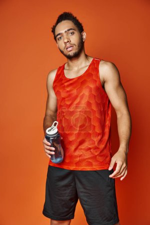 guapo atlético afroamericano hombre en ropa deportiva celebración botella de agua y mirando a la cámara