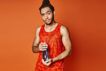 bien parecido atlético afroamericano hombre en ropa deportiva con botella de agua mirando a la cámara