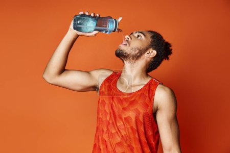 gut aussehender sportlicher afrikanisch-amerikanischer Mann trinkt Süßwasser, während er auf orangefarbenem Hintergrund posiert