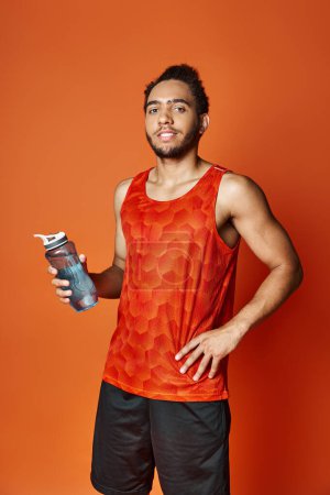 Téléchargez les photos : Séduisant homme afro-américain joyeux en tenue de sport tenant bouteille d'eau et regardant la caméra - en image libre de droit