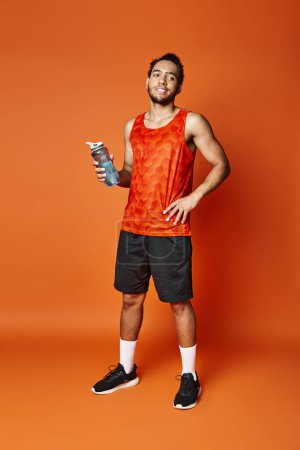schöner athletischer afrikanisch-amerikanischer Mann in lebendiger Sportbekleidung, der eine Wasserflasche in der Hand hält und wegschaut