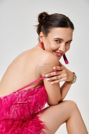 Chica feliz en vestido rosa de moda sostiene correa de su vestido, mirando sexy sobre fondo gris