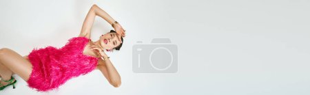 Téléchargez les photos : Portrait de bannière studio de fabuleuse femme brune touchant son visage en robe rose fourrure fantaisie - en image libre de droit