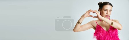Photo for Brunette woman with pierced nose  wearing pink feather dress showing a hand heart to camera, banner - Royalty Free Image