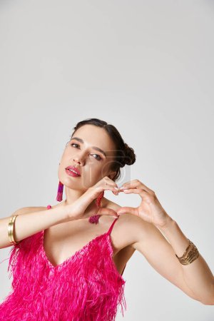 Ruhige hübsche brünette Frau mit durchbohrter Nase, die ein rosafarbenes Federkleid trägt, das ein Handherz zeigt