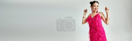 Excited brunette girl in trendy pink outfit beams, dancing on grey background, horizontal banner