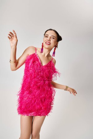 Hübsche Frau in trendigem rosa Kleid und ausgefallenem Schmuck tanzt fröhlich auf grauem Hintergrund