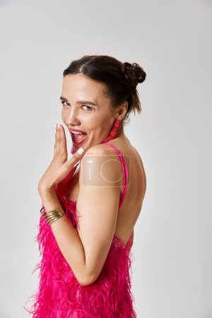 Candid girl in trendy pink outfit smiles naturally, touching her lips gently on grey background