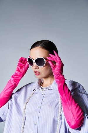 Pretty brunette woman in violet shirt and leather gloves touches her stylish sunglasses