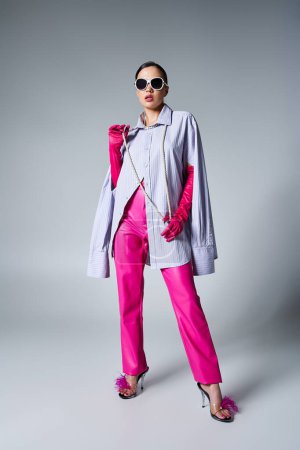 Photo for Stylish brunette woman in pink leather pants and trendy sunglasses touching pearls on neck - Royalty Free Image