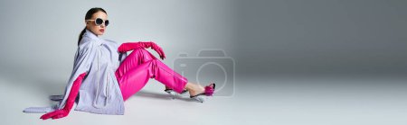Pretty woman in pink gloves, leather pants and chic sunglasses sitting on grey background, banner