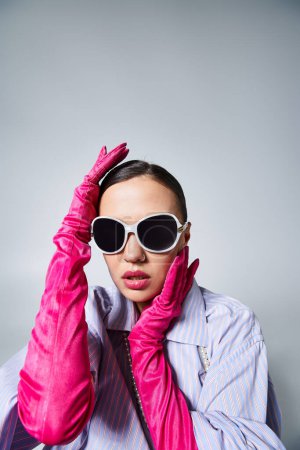 Brunette woman with chic pink gloves elegantly touching her face, wearing sunglasses and pearls