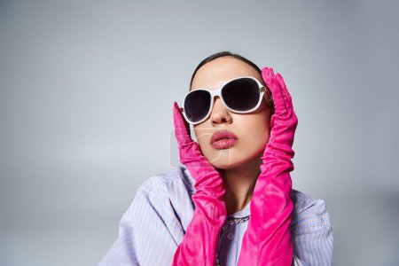 Attraktive Frau in violettem Hemd und Perlen, trägt Sonnenbrille und berührt ihr Gesicht sanft