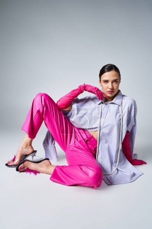 Attractive woman in pink pants and gloves, violet shirt, sitting confidently and touching her chin
