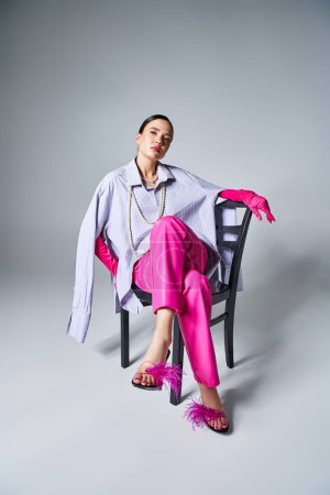 Pretty brunette woman wearing pink gloves and stylish pants, sitting on chair and looking confident