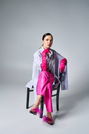 Photo for Confident brunette girl wearing pink gloves, feather shoes and stylish pants, sitting on chair - Royalty Free Image