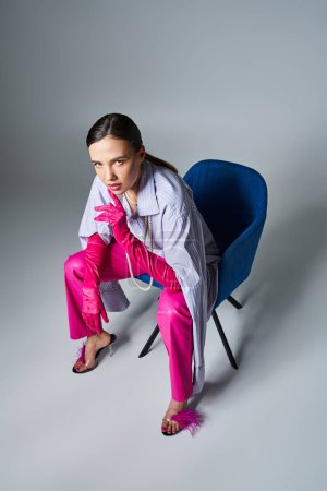 Photo for Pretty woman in stylish outfit and chic gloves, sitting on chair, touching her face - Royalty Free Image