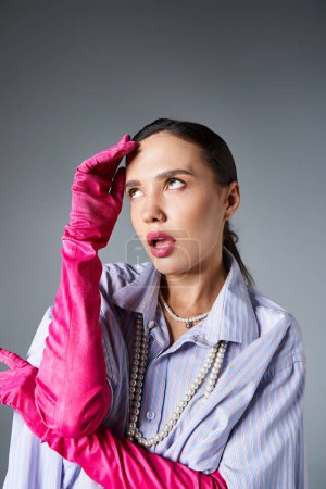 Woman with piercing in stylish outfit and pink gloves, touches her face looking away
