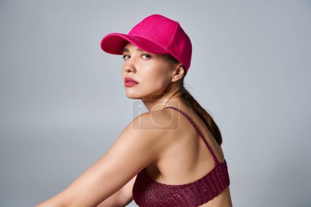 Back view of woman in knitted bordeax top and pink cap sitting on grey background