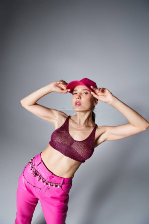 Fancy brunette woman in knitted top and pink trousers touching pink cap with one hand