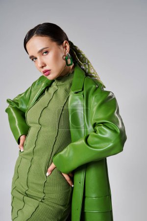Fashionable woman in total green trendy look on grey background posing with hands on waist
