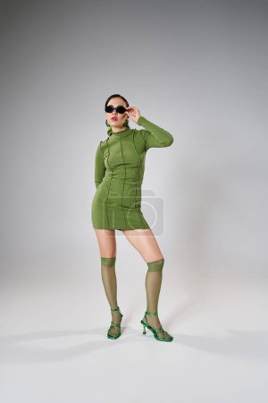 Téléchargez les photos : Photo pleine longueur d'une femme élégante portant une tenue verte et des lunettes de soleil touchantes avec une main - en image libre de droit