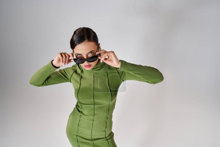 Téléchargez les photos : Vue du dessus de la femme en tenue verte, touchant ses lunettes avec les deux mains et regardant la caméra - en image libre de droit