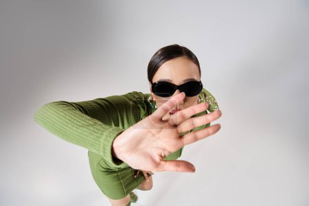 Top view of woman in green outfit and sunglasses, covering her face with hand and looking at camera