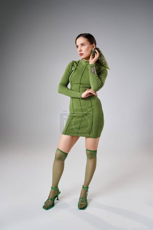 Brunette woman in green mini dress, knee socks and shoes, wearing stylish jewelry, hands on her body