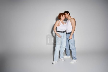 atractivo sexy pareja en azul jeans posando juntos amorosamente sobre gris fondo, relación