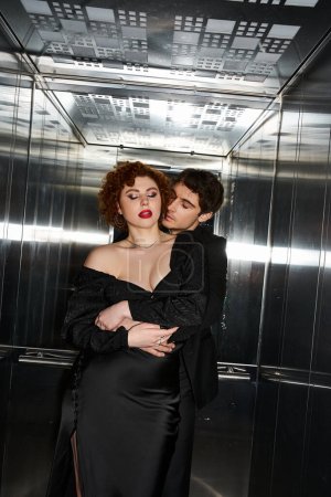 Téléchargez les photos : Tentant amour petit ami et petite amie dans élégant noir vêtements câlins dans l'ascenseur, couple sexy - en image libre de droit