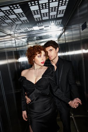 sexy verführerisches Paar in elegantem schwarzen Kleid und Anzug, das sich nach dem Date liebevoll im Fahrstuhl umarmt