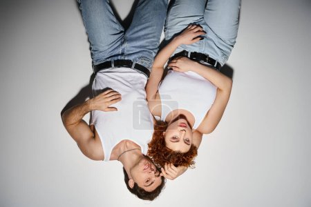 alluring man and woman in blue jeans lying on floor together and looking at camera, sexy couple