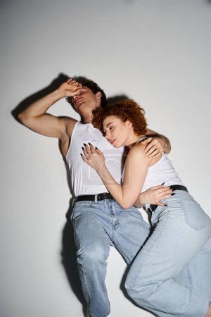 Téléchargez les photos : Beau couple séduisant en jean bleu décontracté couché sur le sol ensemble et étreignant chaleureusement - en image libre de droit