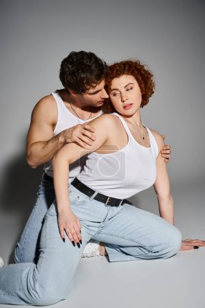 charming man and woman in blue jeans sitting on floor together and hugging warmly, sexy couple