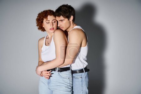 Téléchargez les photos : Attrayant petit ami et petite amie en tenue décontractée étreignant amoureusement sur fond gris, couple sexy - en image libre de droit