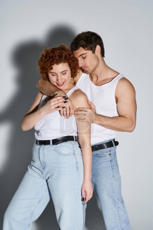 Téléchargez les photos : Joyeux séduisant homme et femme en jeans posant sur fond gris et souriant heureux, couple sexy - en image libre de droit