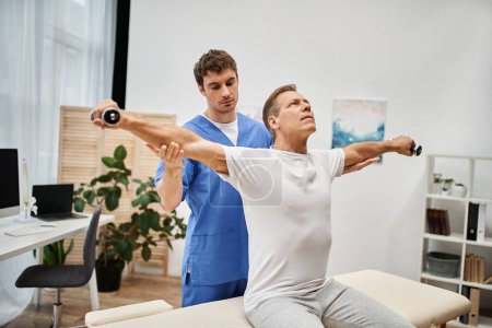 mature patient in casual attire using dumbbells with help of his dedicated doctor, rehabilitation